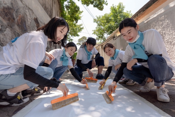 25일 대우건설 대학생 홍보대사들이 서울시 성북구에 위치한 노후주택에 도배할 벽지에 풀을 바르고 있다.